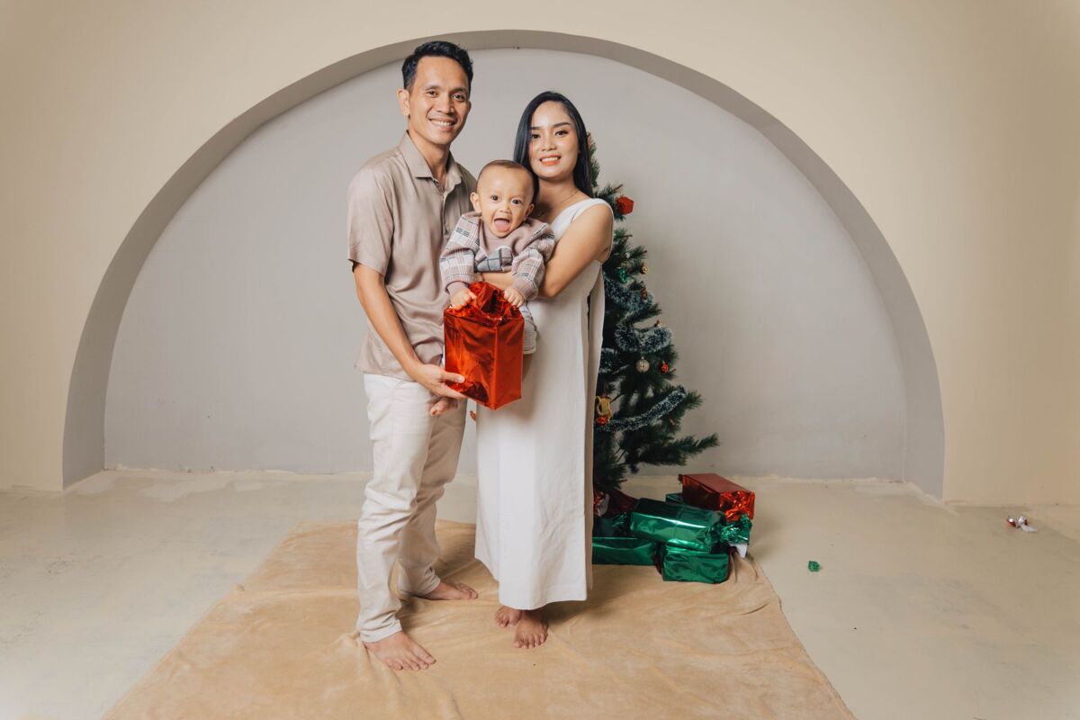 A joyful family posing with gifts by a Christmas tree indoors, capturing holiday spirit.