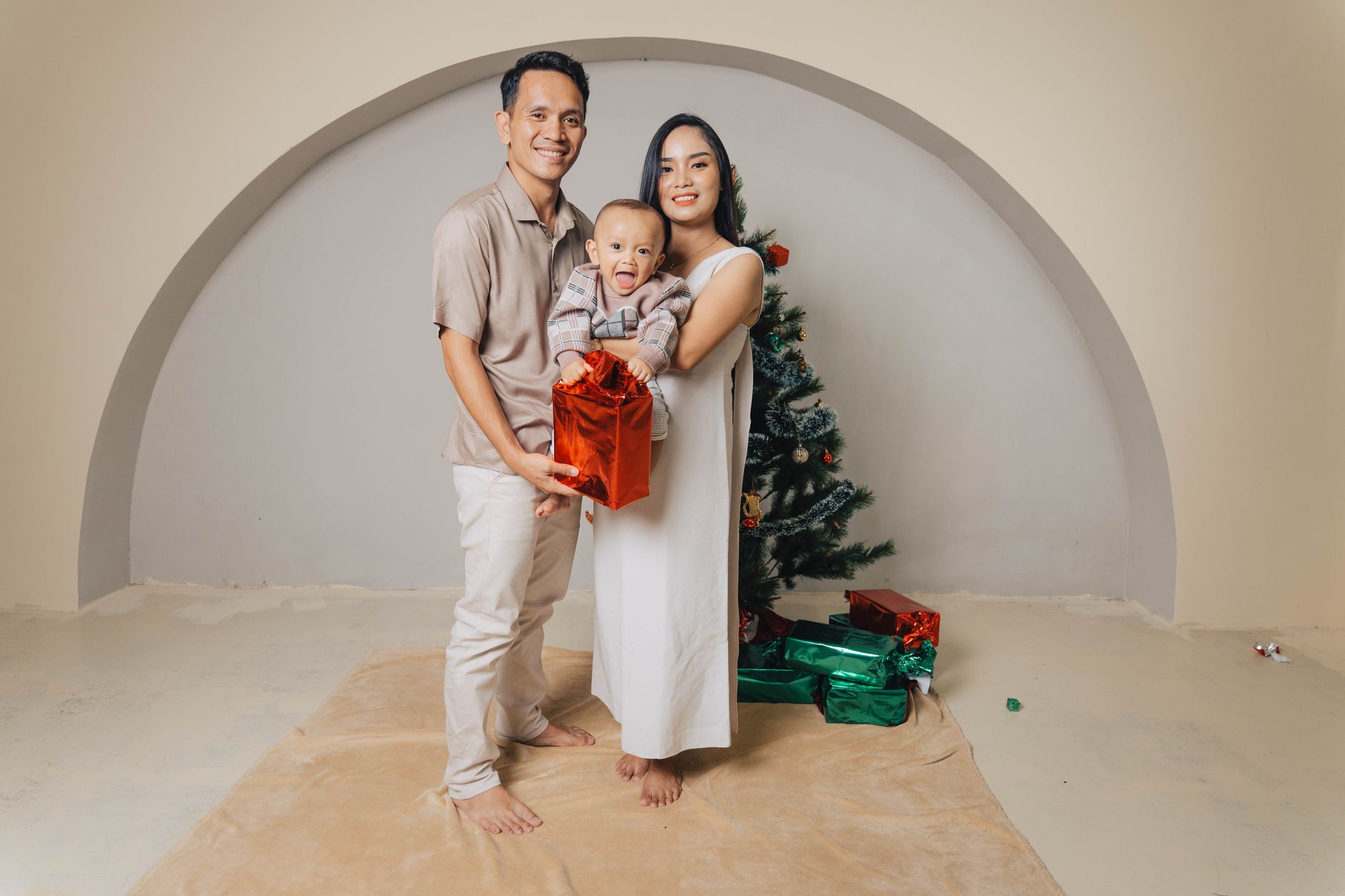 A joyful family posing with gifts by a Christmas tree indoors, capturing holiday spirit.