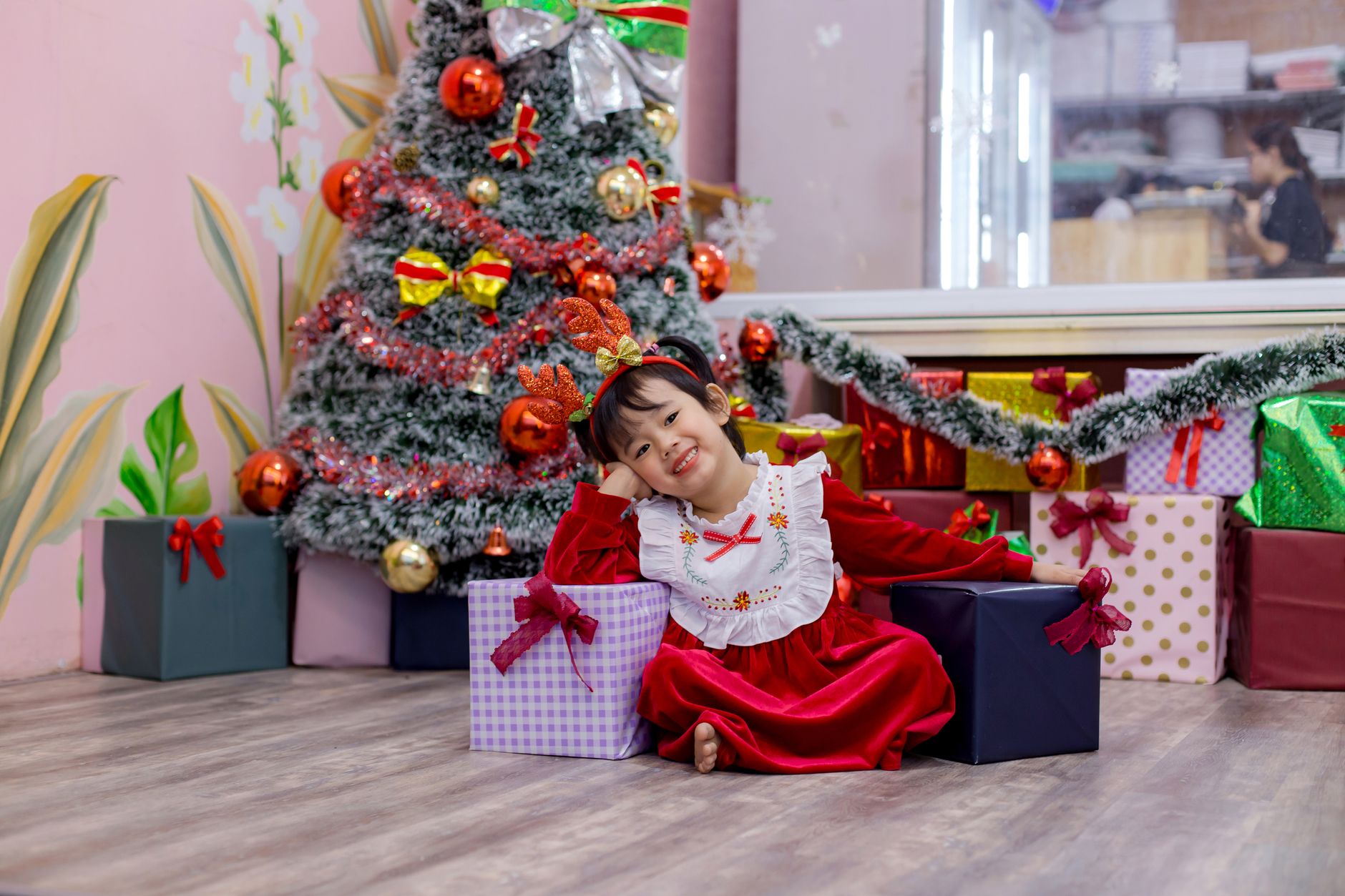 Happy child in festive attire sitting by a decorated Christmas tree in Hoi An, Vietnam.