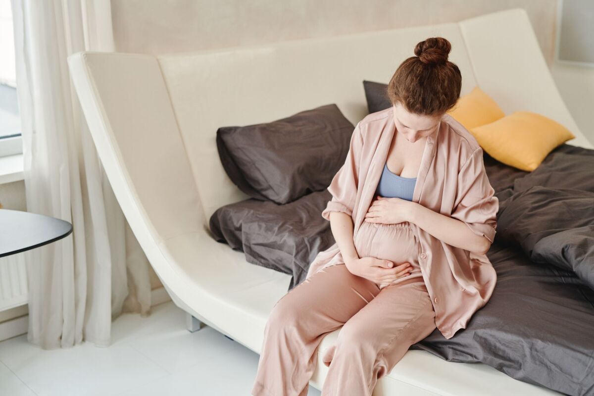 A pregnant woman sitting on a bed, embracing her belly in a cozy and modern bedroom setting.