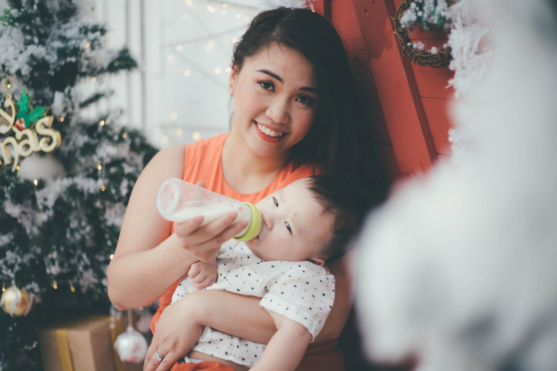 An Asian mother happily feeds her baby with a bottle during the Christmas holiday season.