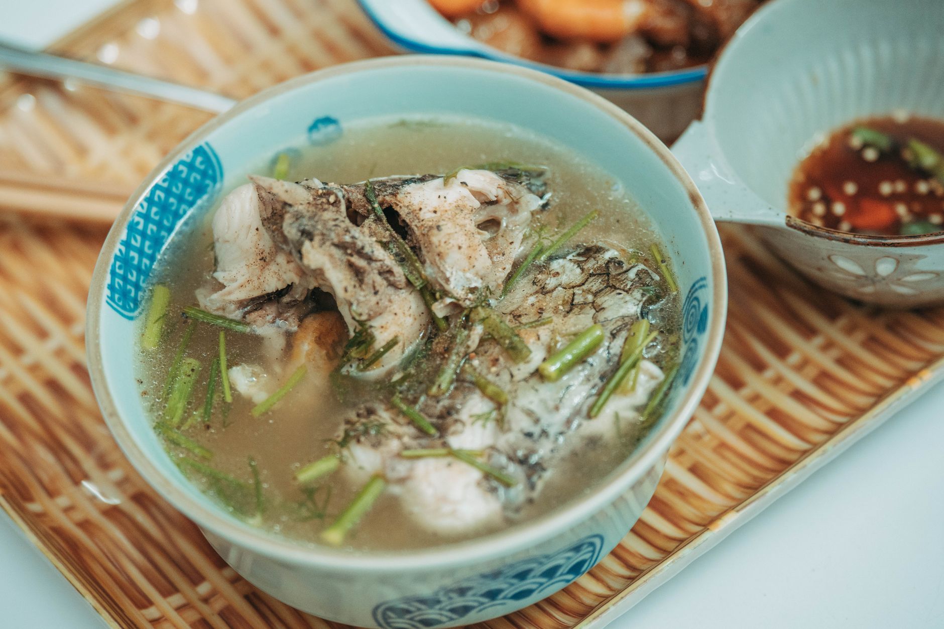 A steaming bowl of fish soup garnished with herbs served in a traditional ceramic bowl on a bamboo tray.