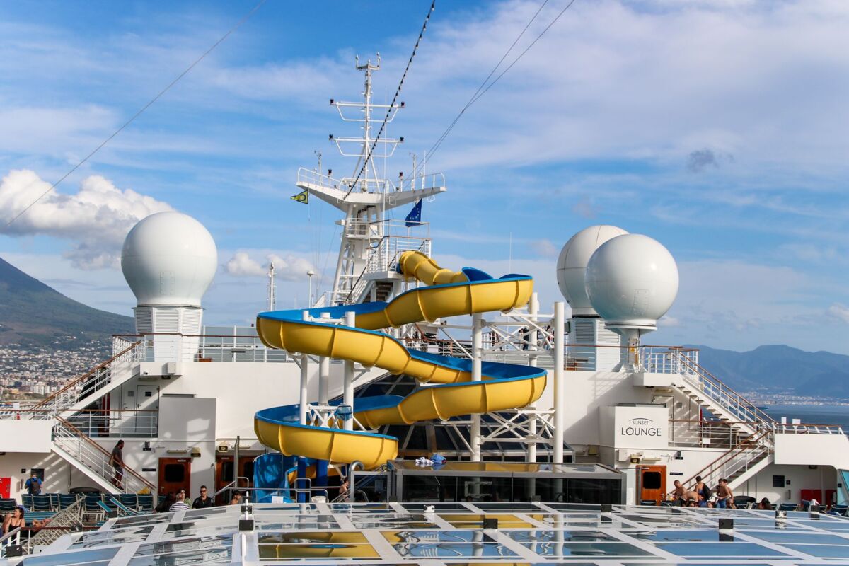 View of a cruise ship deck featuring a vibrant yellow waterslide against a scenic ocean backdrop.