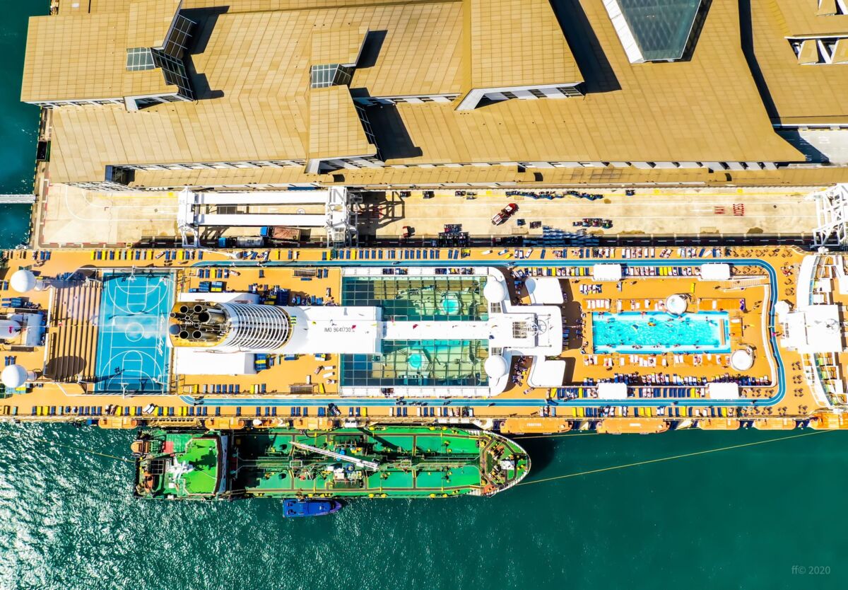 Top-down aerial view of cruise ship at Singapore harbor with pools and lounging area.