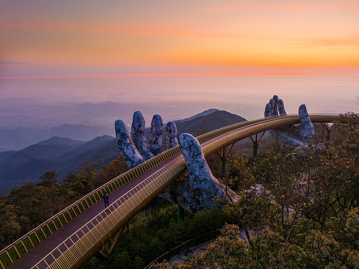 The Golden Bridge held up by giant stone hands above the mountains of Ba Na Hills near Da Nang at sunset