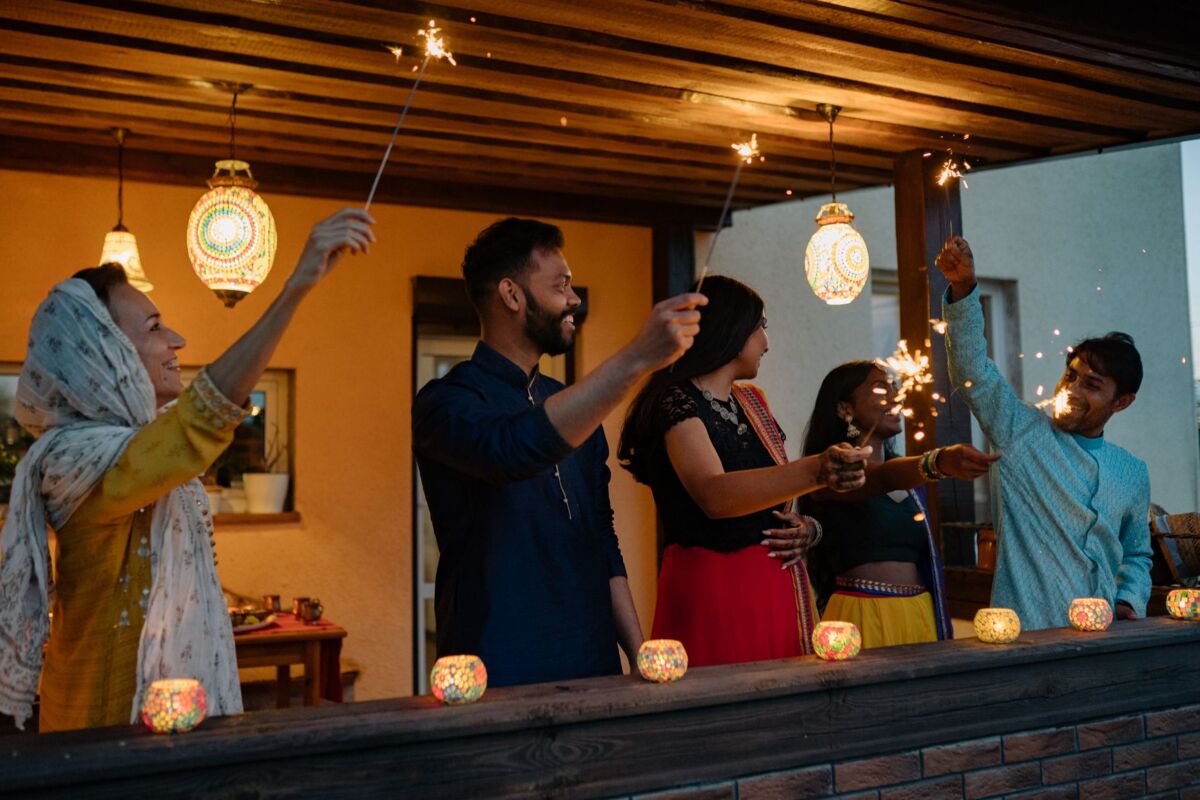 Happy group of friends celebrating Diwali with sparklers in traditional attire on a decorated balcony.