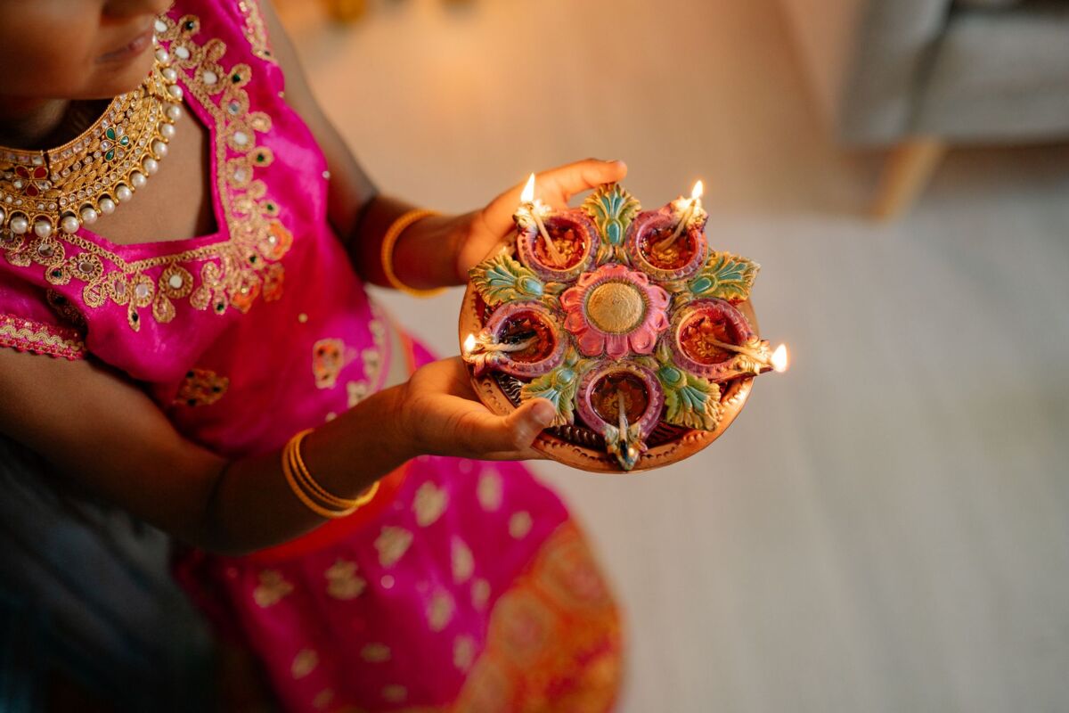 A young girl in traditional attire holds decorative Diwali lamps, spreading light and celebration.