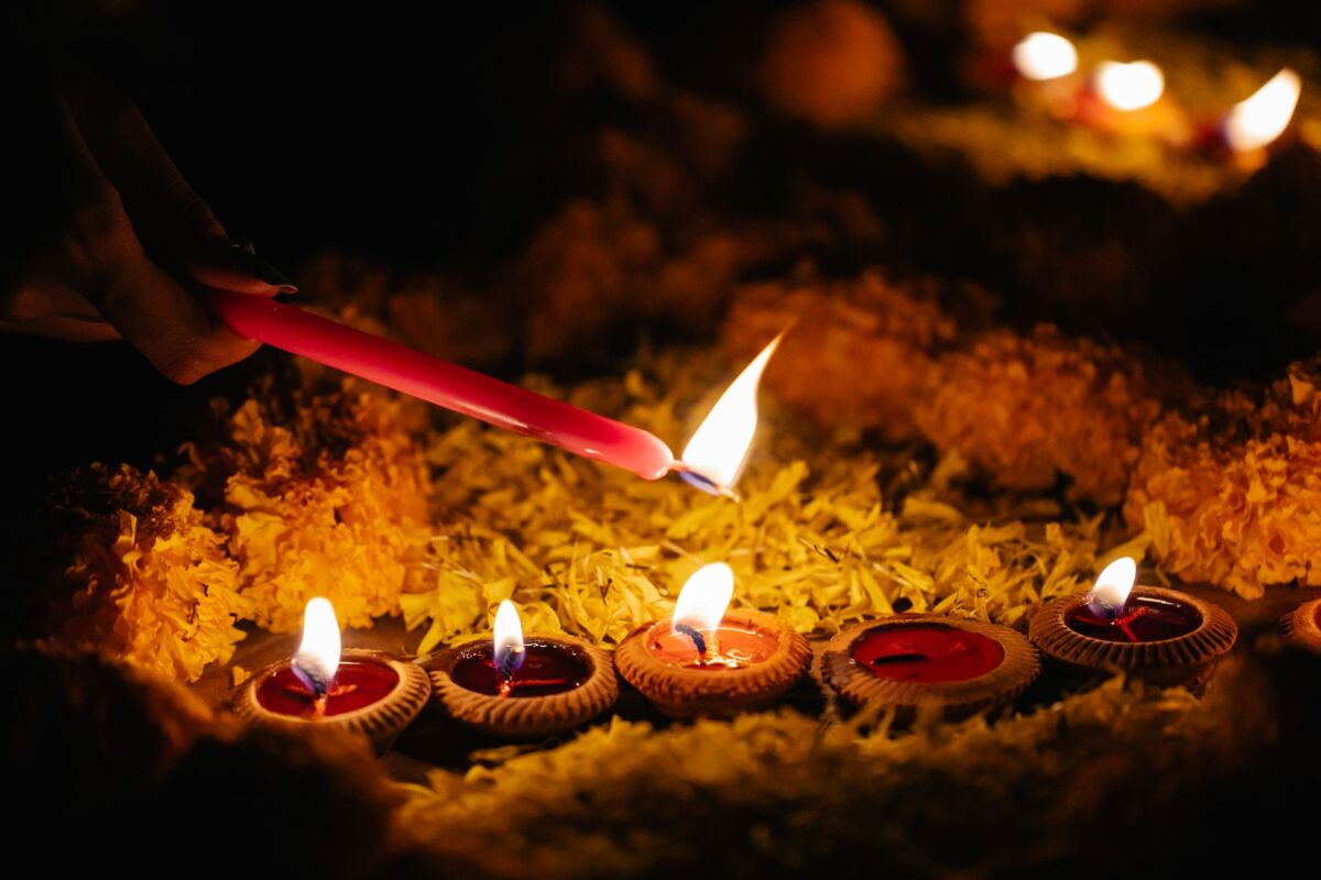 Close-up of hand lighting colorful candles surrounded by marigolds, creating a warm festival ambiance.