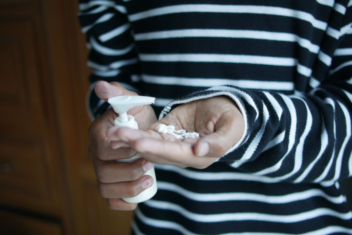 Close up of hands applying cream from a bottle, wearing a striped shirt.