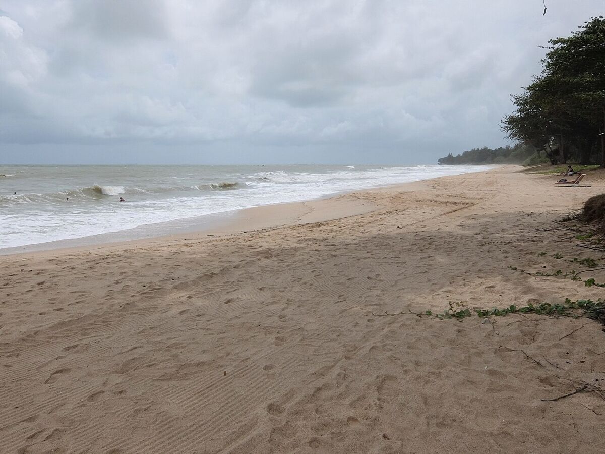 Wide open stretch of Desaru Beach with rolling waves, a sun lounger and casuarina trees along the shore