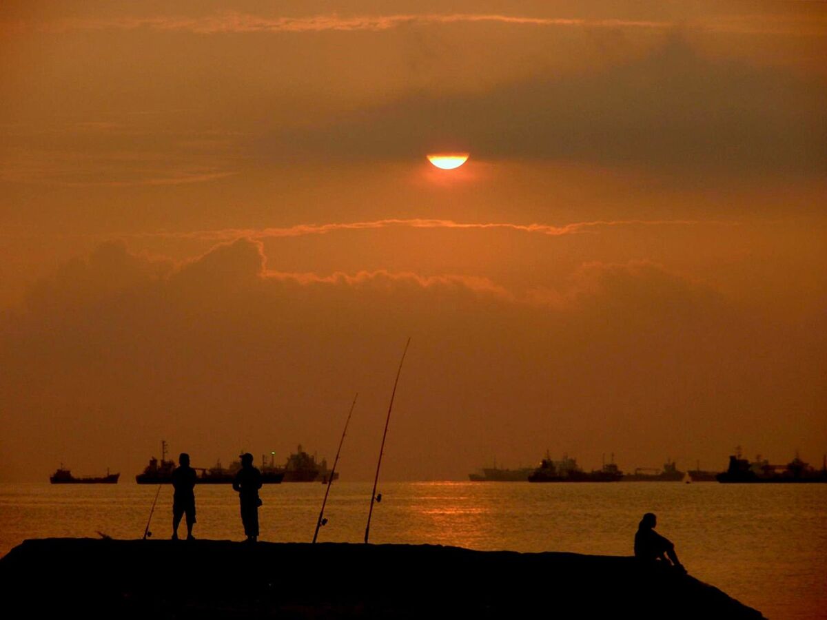 Orange sunrise over the sea at East Coast Park with anglers fishing and cargo ships on the horizon