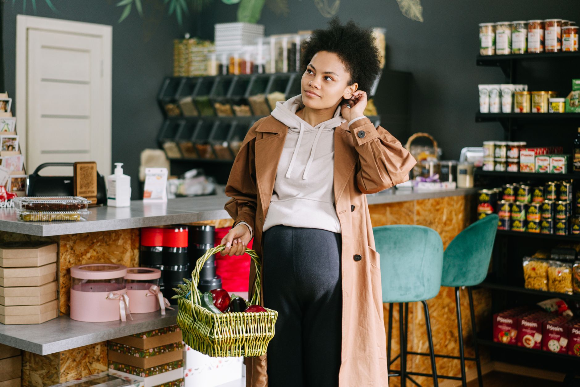 Pregnant woman holding a basket of groceries in a cozy grocery store.