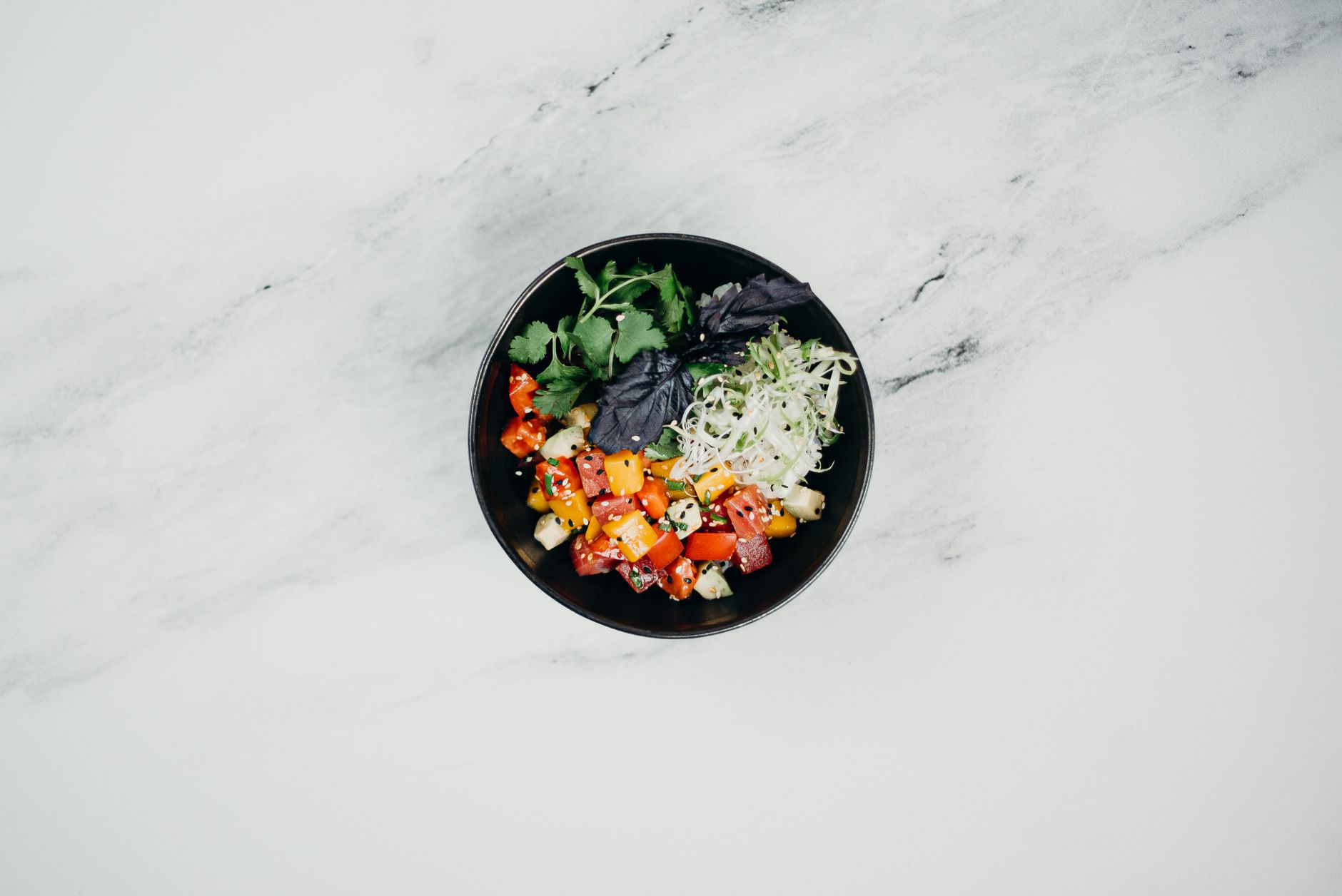 A vibrant vegetable salad with fresh herbs served in a black bowl on a marble surface, perfect for healthy eating.