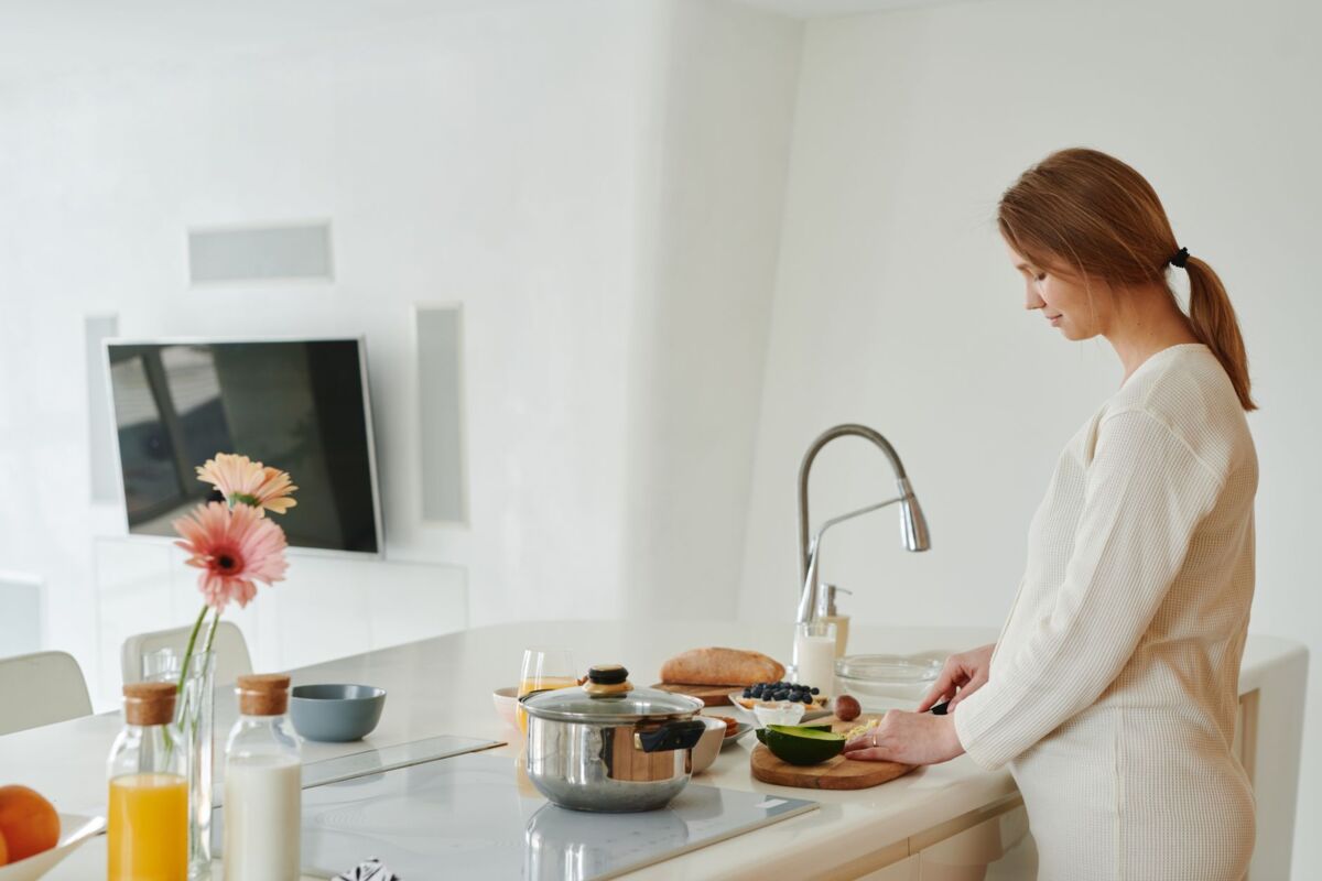 A pregnant woman slices avocado in a contemporary kitchen. Healthy and serene lifestyle.