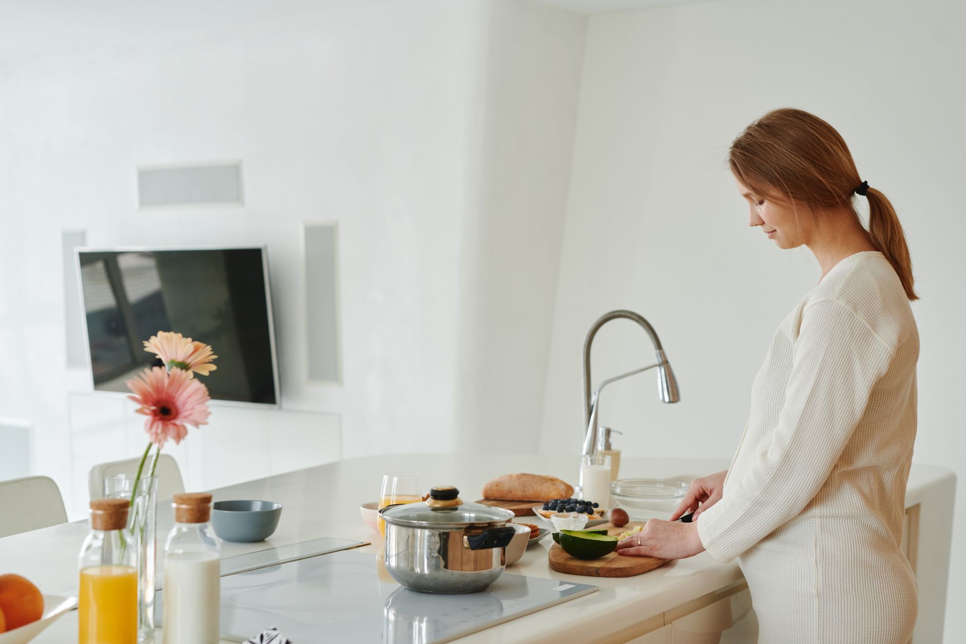 A pregnant woman slices avocado in a contemporary kitchen. Healthy and serene lifestyle.