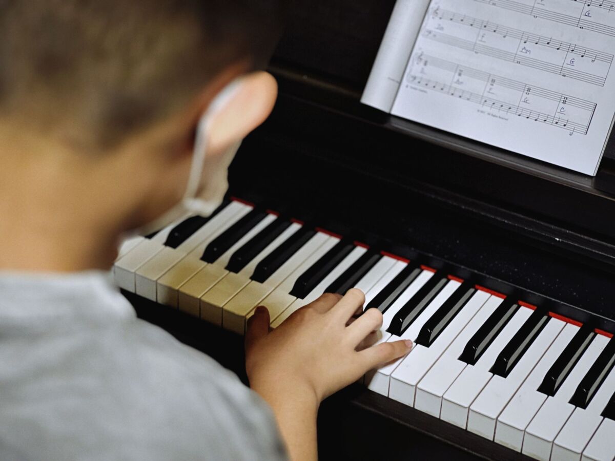 Young child learning to play piano with open sheet music, focusing on keys.
