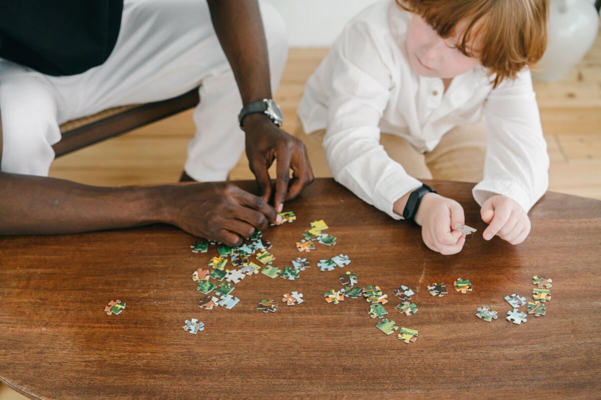 Adult and child bonding while solving a puzzle on a wooden table.