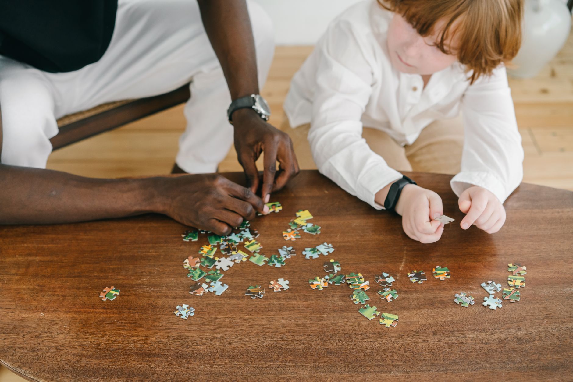 Adult and child bonding while solving a puzzle on a wooden table.
