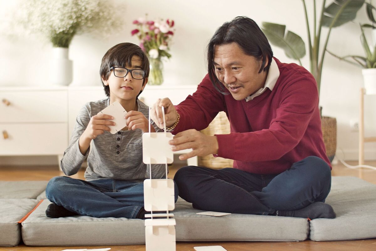Asian father and son bonding by building a card tower indoors. Fun and creativity at home.