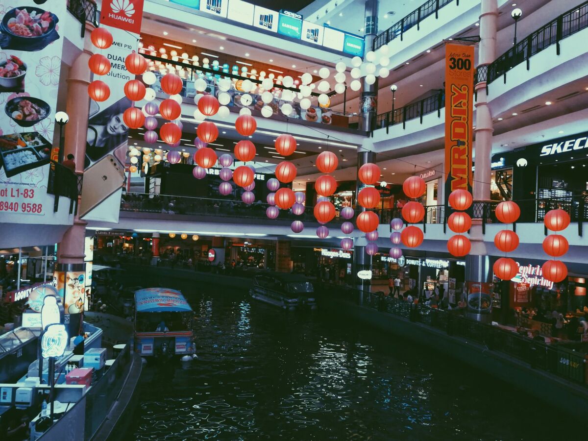 Colorful lanterns decorate an indoor mall with waterway and boats, creating a lively shopping atmosphere.