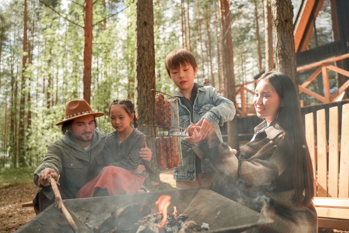 A family of four enjoying grilling by a campfire in a forest setting, capturing the essence of outdoor adventure.