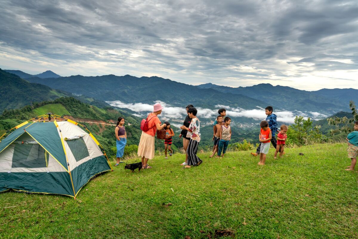 Group of children playing by a tent on a grassy hillside with stunning mountain views.