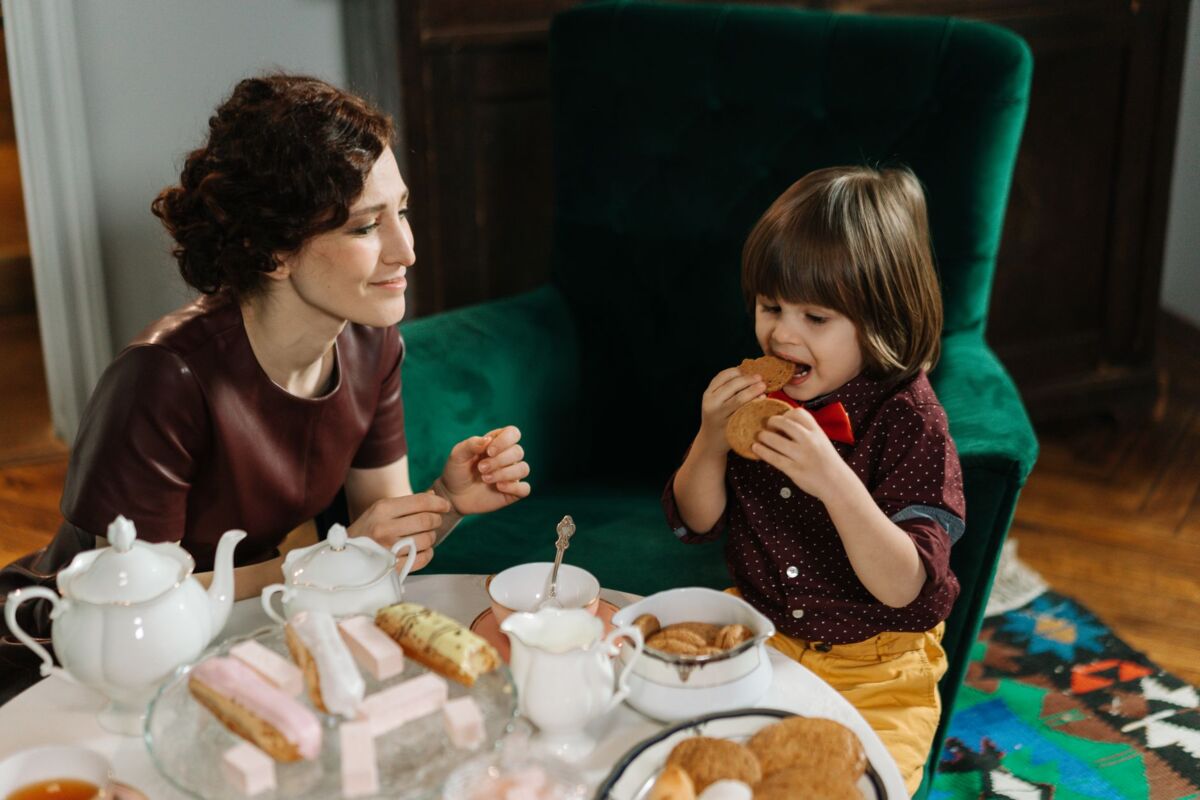 Mother and son sharing a special tea time with pastries and cookies in a cozy living room setting.
