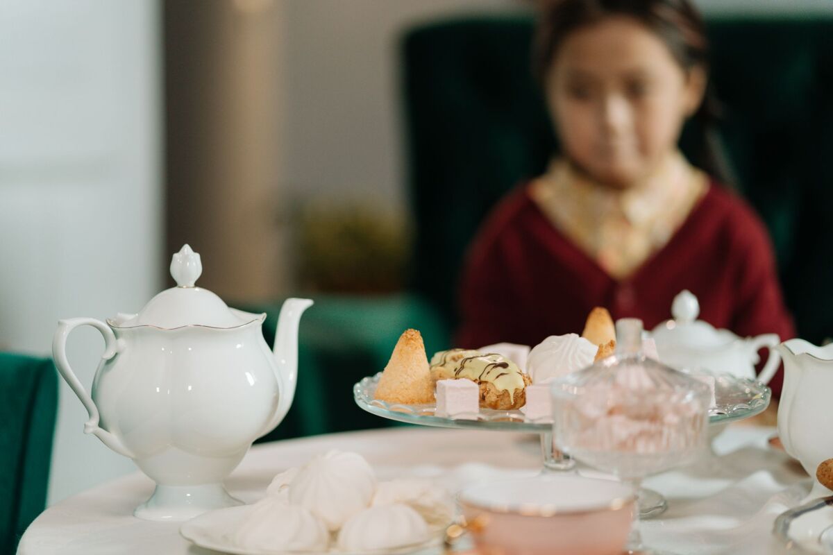 A beautifully set tea table with a young girl, featuring a variety of desserts and a classic tea pot.