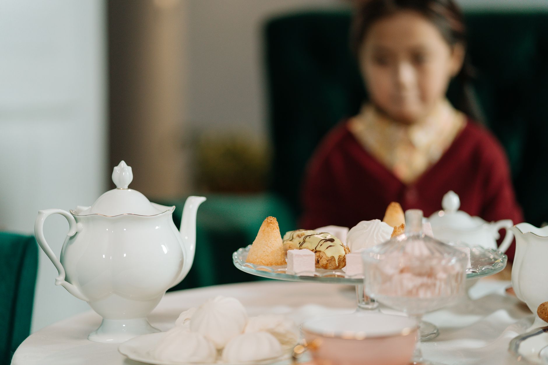 A beautifully set tea table with a young girl, featuring a variety of desserts and a classic tea pot.