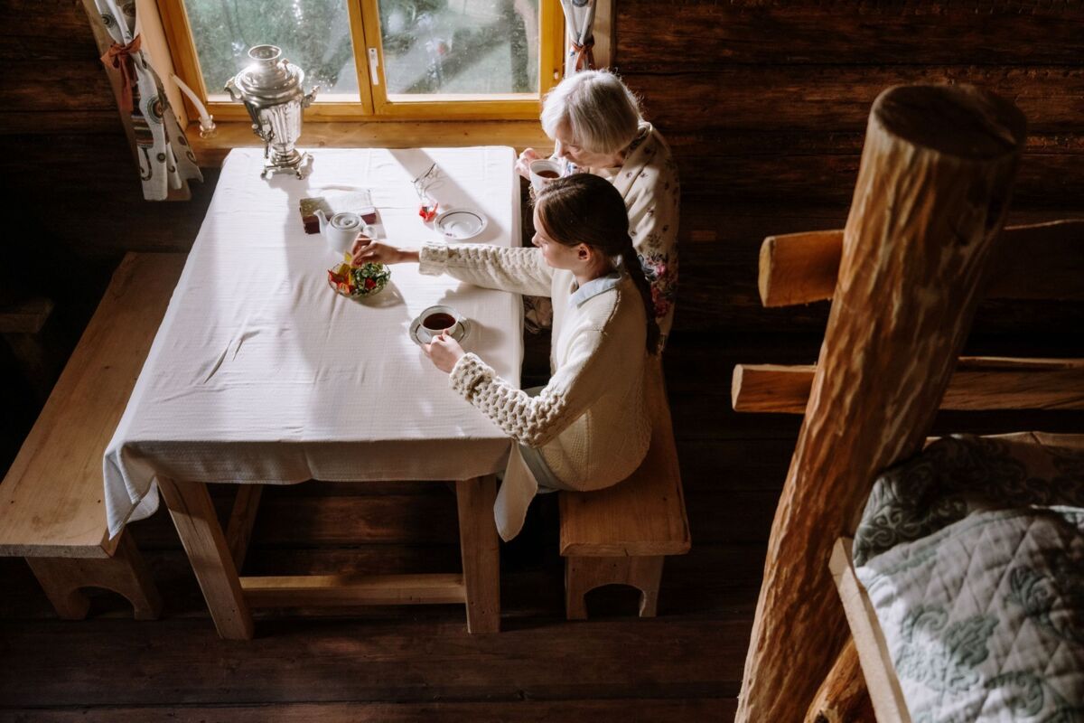 Grandmother and granddaughter enjoying tea together indoors in a cozy cabin setting from a high angle.