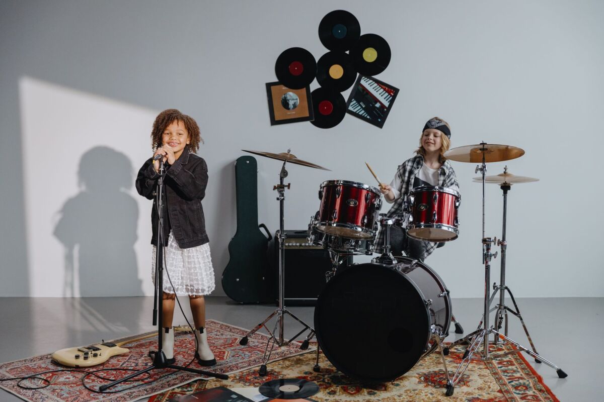 Children singing and drumming joyfully in a music studio with instruments.