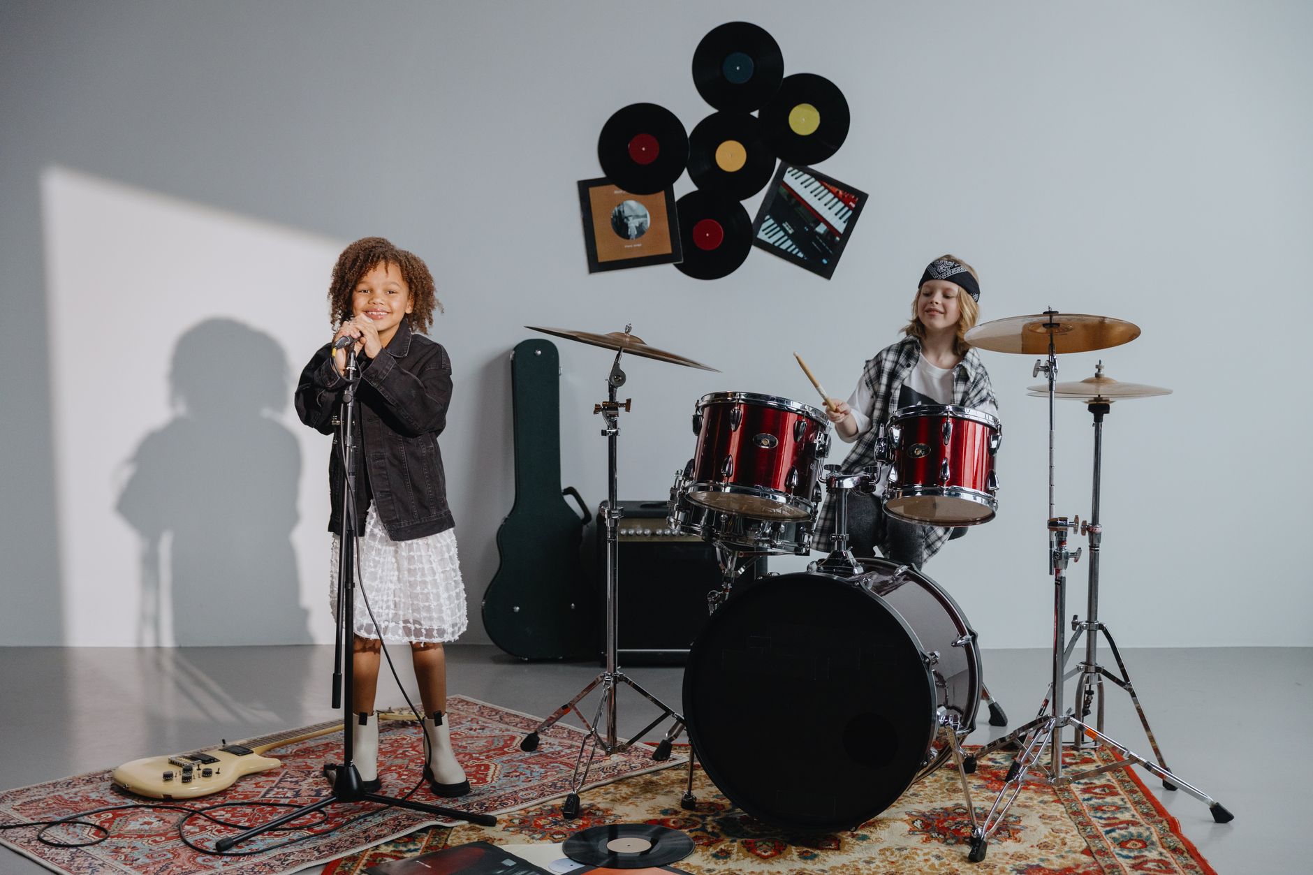 Children singing and drumming joyfully in a music studio with instruments.