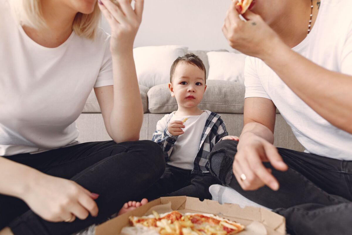 A young child and parents enjoying pizza indoors in a casual family setting.