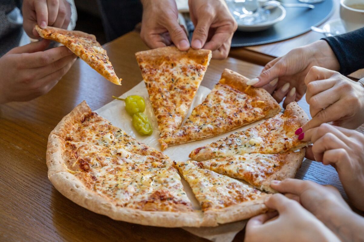 Multiple hands reaching for pizza slices on a cozy restaurant table.