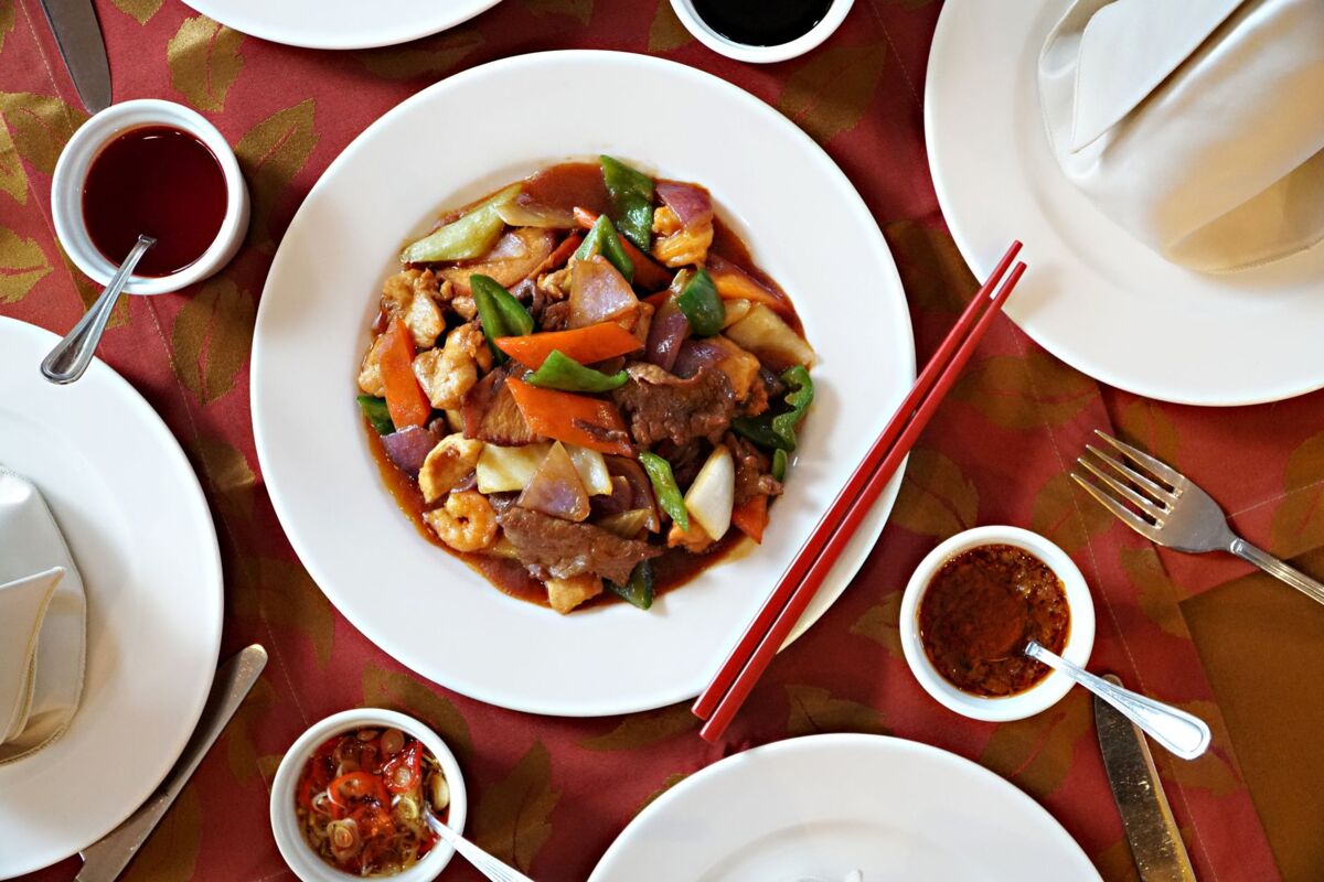 A vibrant stir-fry dish featuring vegetables and meats served with red chopsticks on a restaurant table.