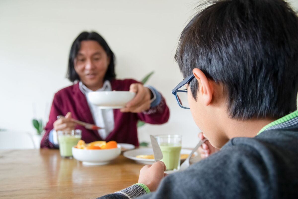 Asian father and son enjoying a healthy breakfast together at home in Portugal.