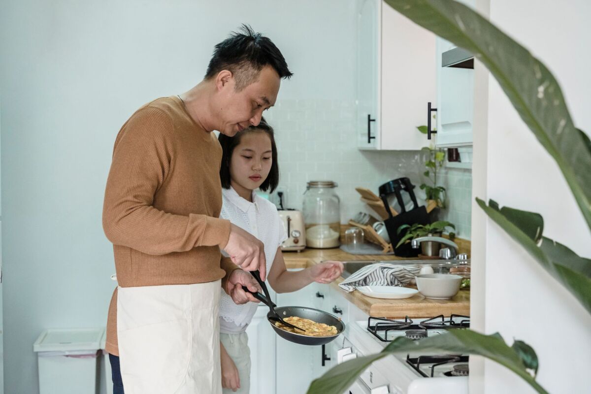 A father and his daughter cooking scrambled eggs together in their kitchen.