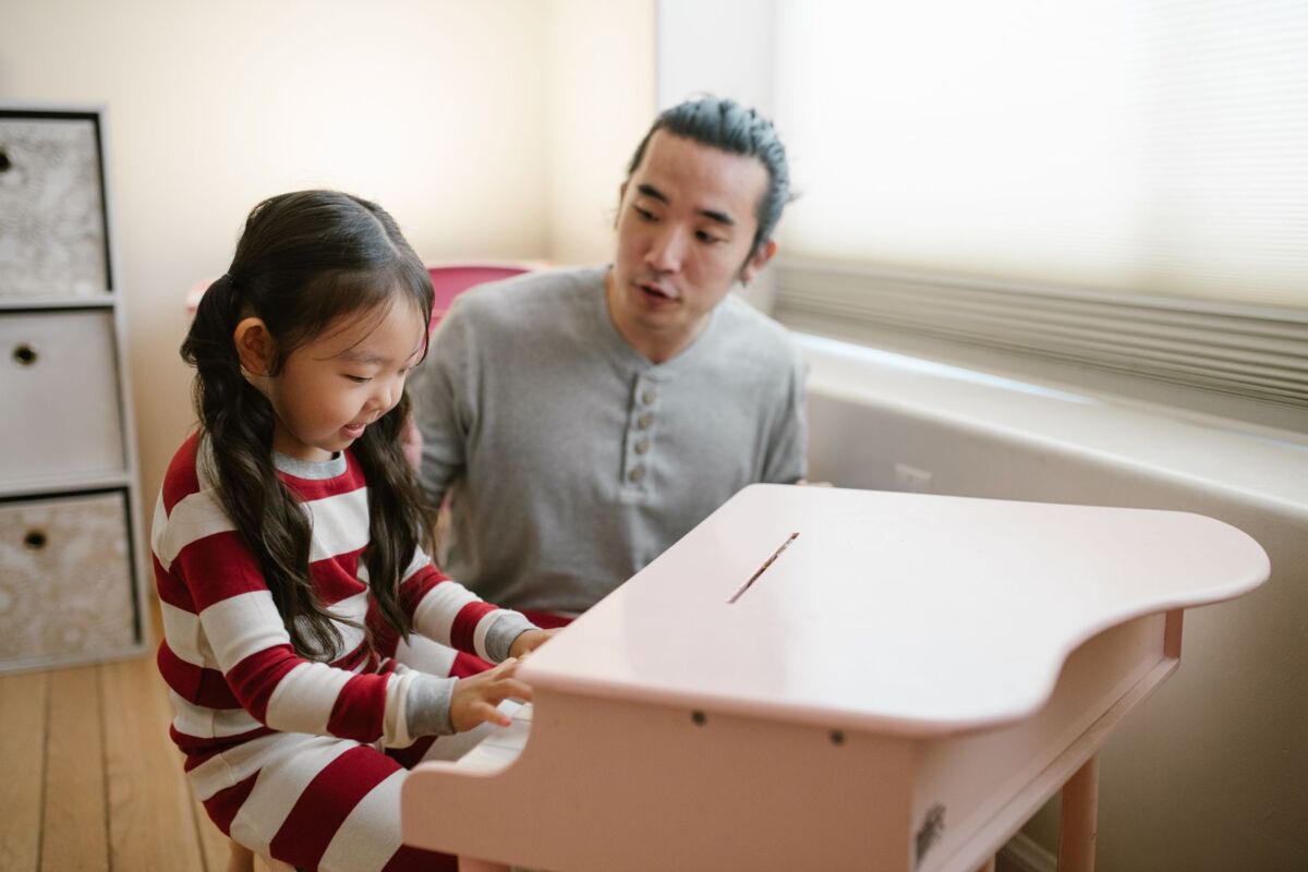 Father guiding daughter at the piano, capturing a bonding moment in a cozy home setting.