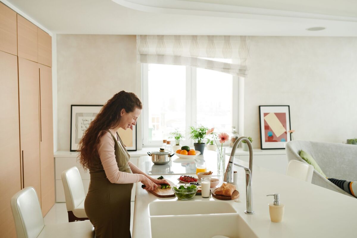 Pregnant woman slicing vegetables in a bright kitchen setting, embracing healthy lifestyle.