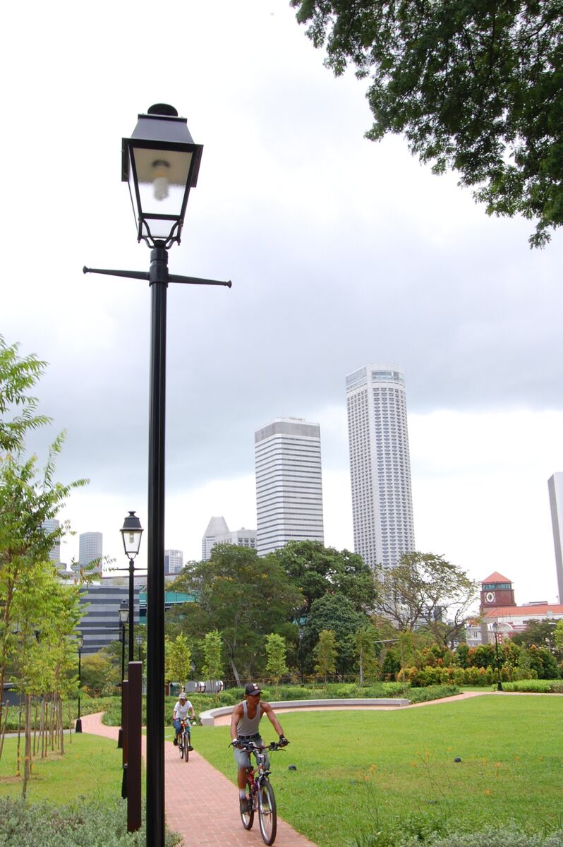 Cyclists riding a brick path through Fort Canning Park lawns with the city skyline behind