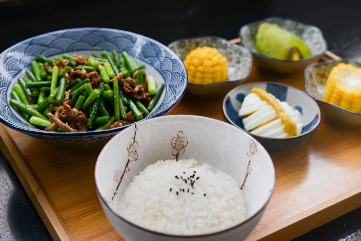 A vibrant Asian meal featuring rice, green beans, corn, and more on a wooden tray.