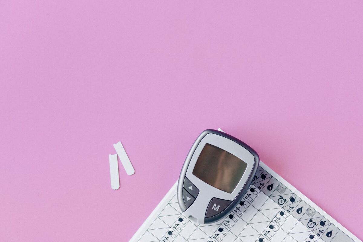 Flat lay of a blood glucose monitor and test strips on a pink surface.
