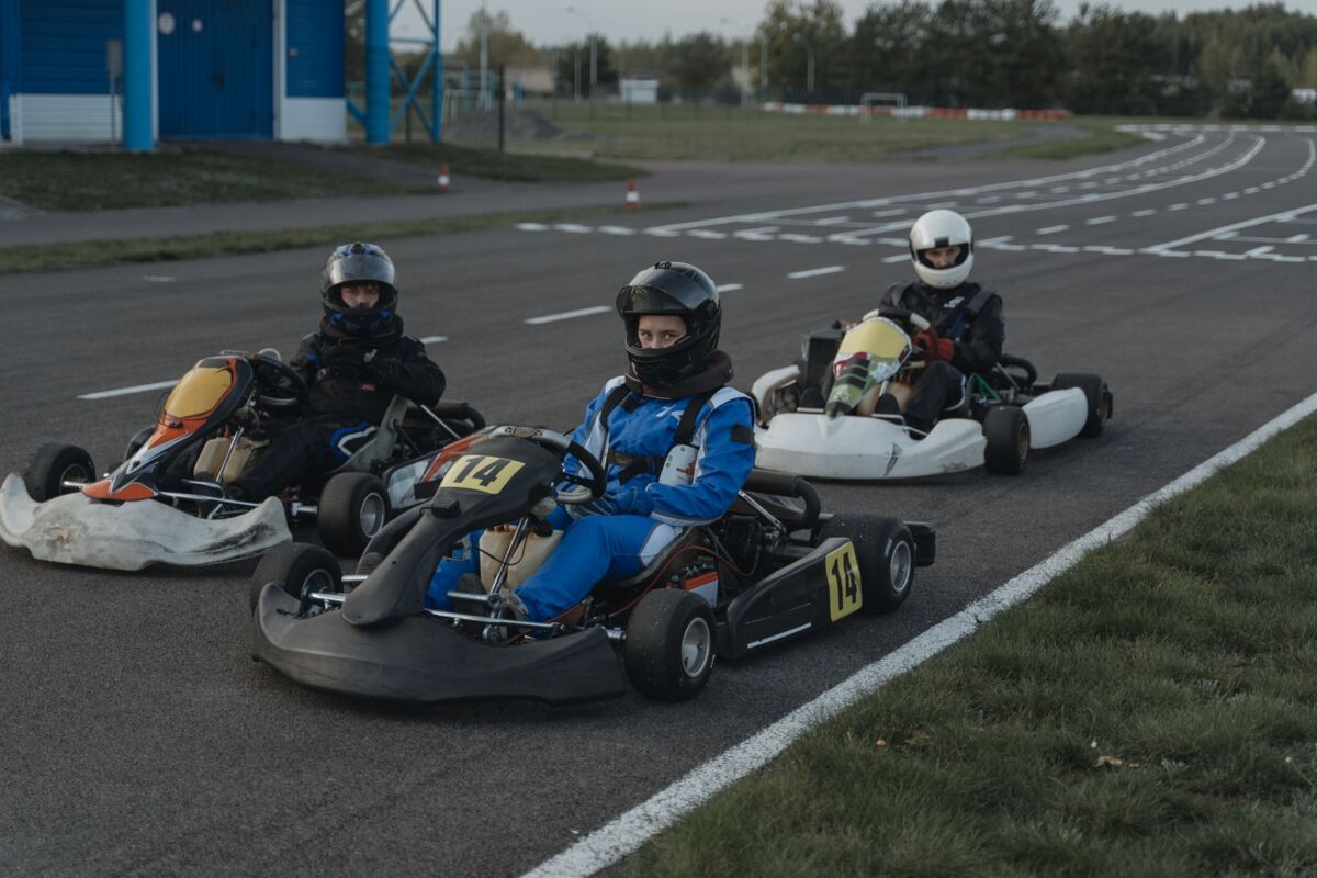 Three go-kart racers in protective gear sit ready on a racing track.