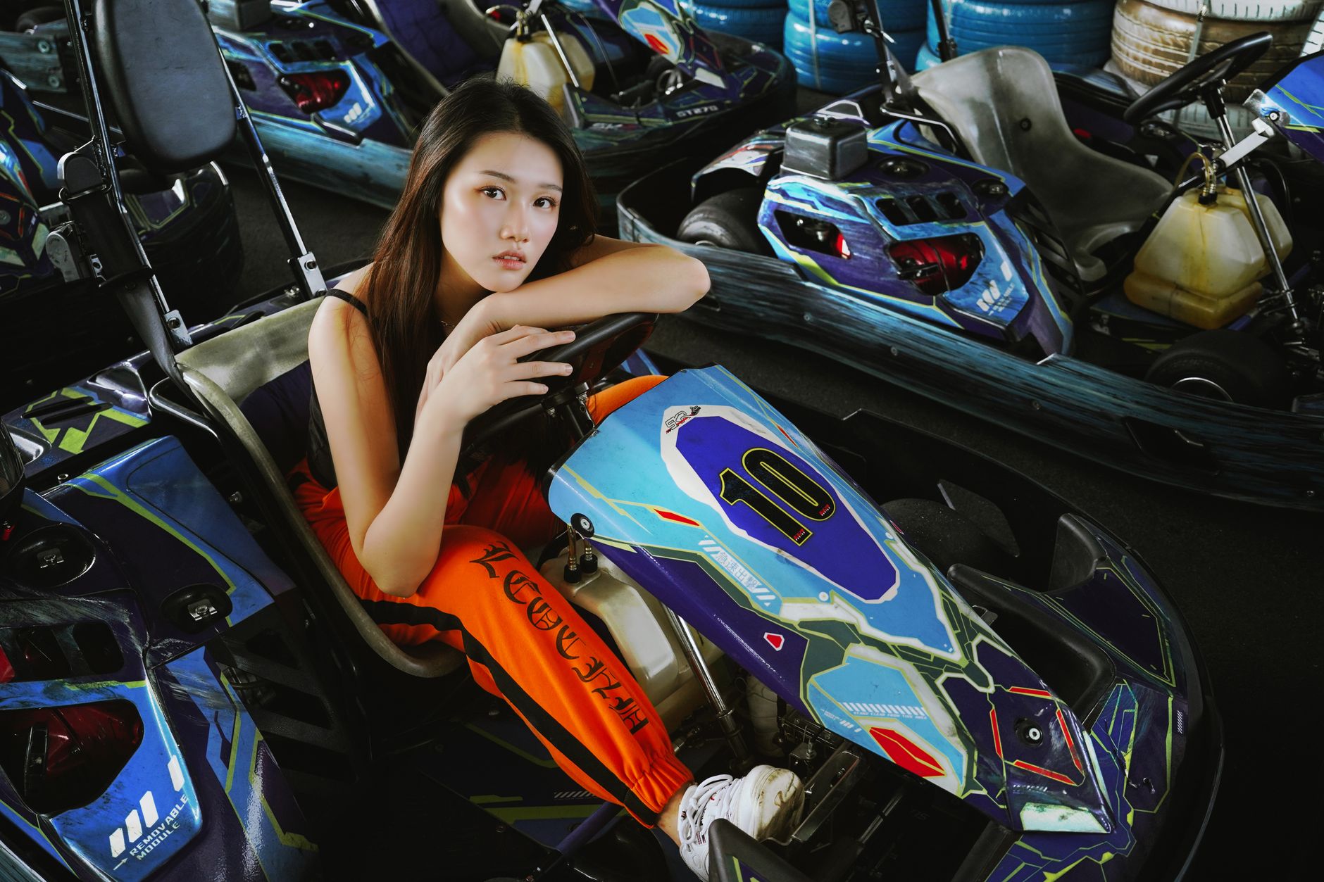 Portrait of a young woman sitting in a go-kart on an indoor track, with vibrant colors and a focused expression.