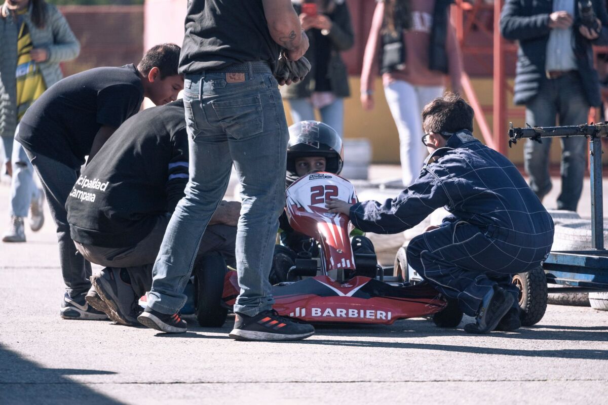 Child racer getting ready on an outdoor go-kart track with a team of supporters.