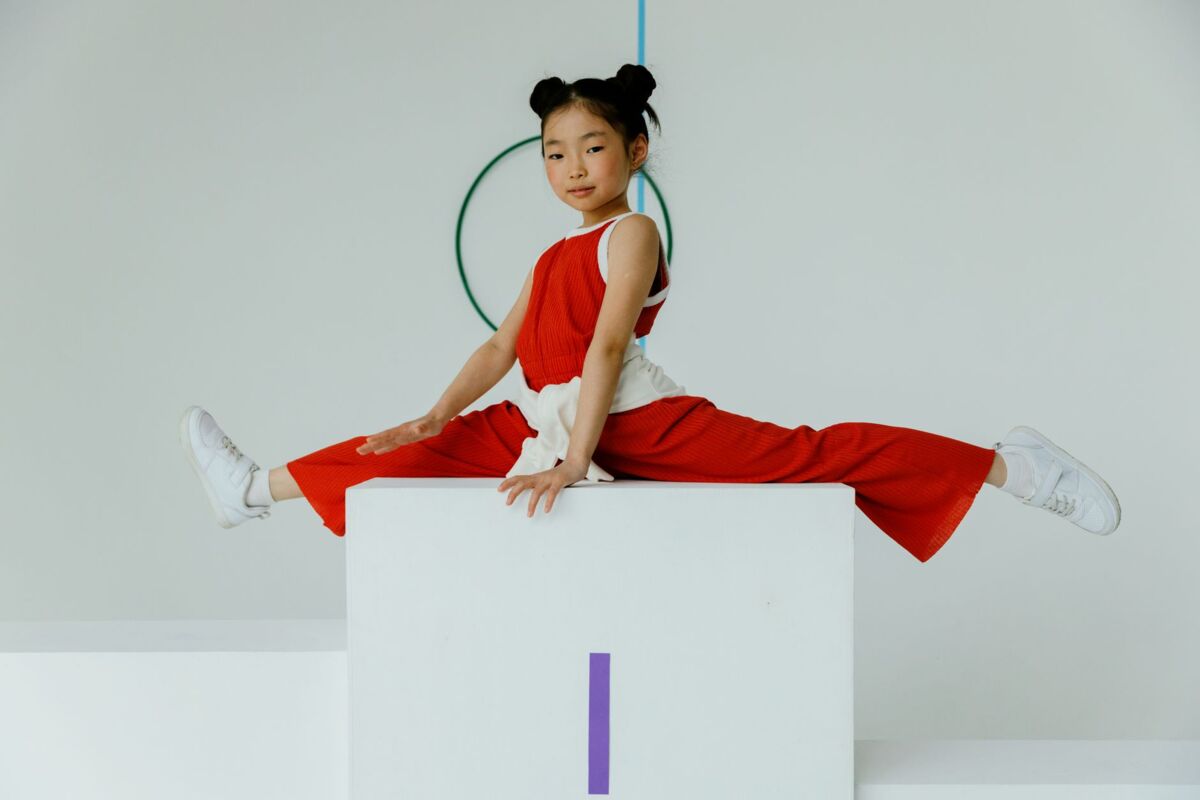 A child gymnast performs a perfect split on a podium indoors, showcasing flexibility.