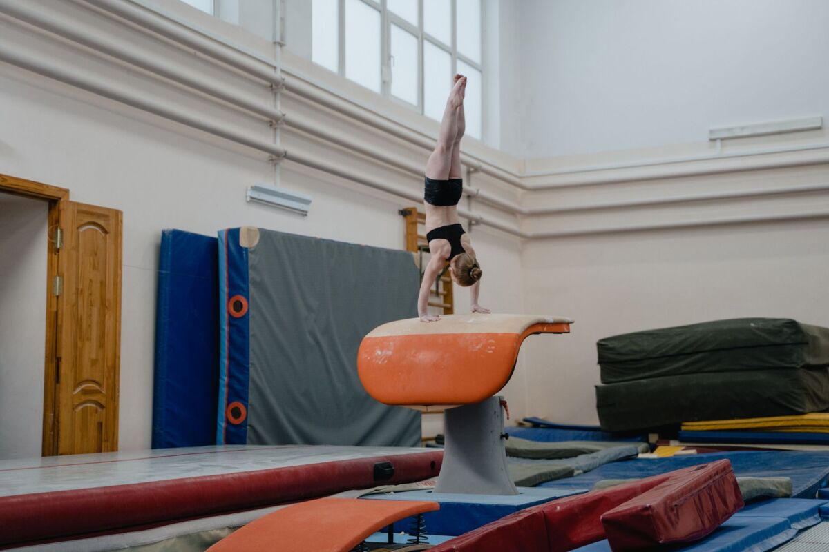 A girl practicing a handstand on vault in an indoor gymnasium setting.