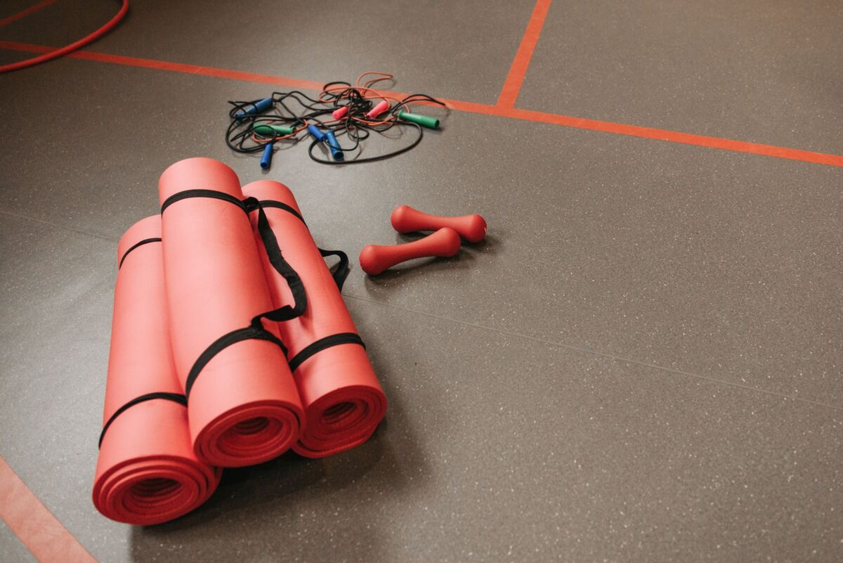 Red yoga mats, jump ropes, and dumbbells neatly arranged on a gym floor for fitness activities.
