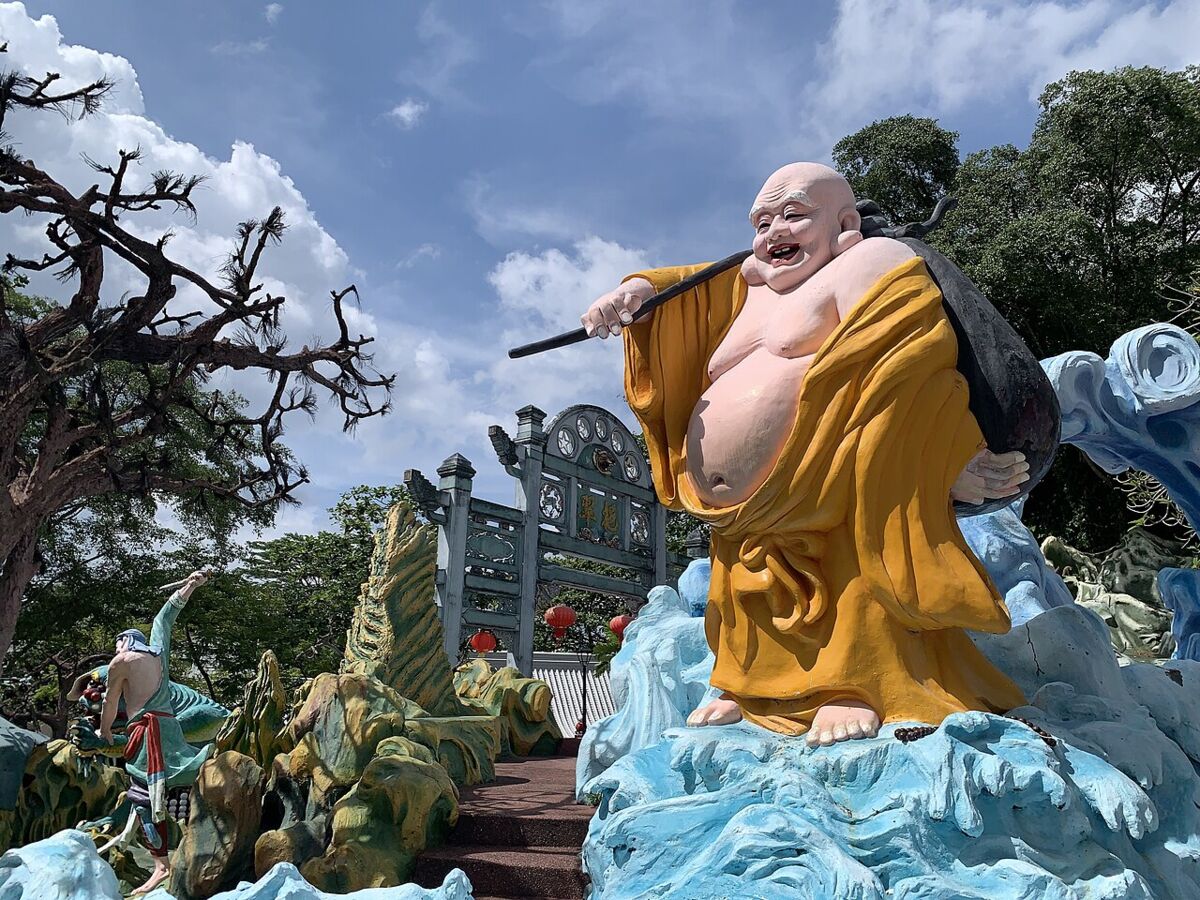 Giant laughing Buddha statue in golden robes amid blue waves and rockwork at Haw Par Villa, Singapore