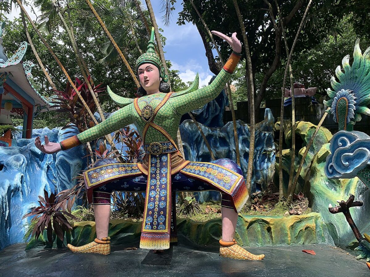 Brightly painted green-robed deity statue in a dancing pose among colourful rockwork at Haw Par Villa